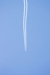 Low angle view of vapor trails against clear blue sky