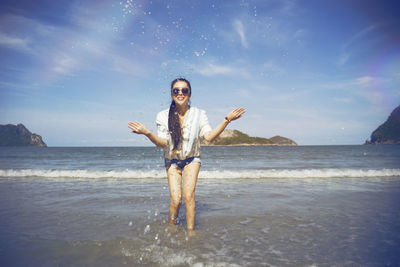 Portrait of woman wearing sunglasses splashing water in sea