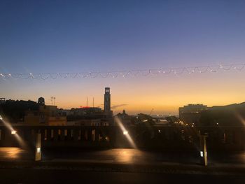 Illuminated city buildings against clear sky during sunset