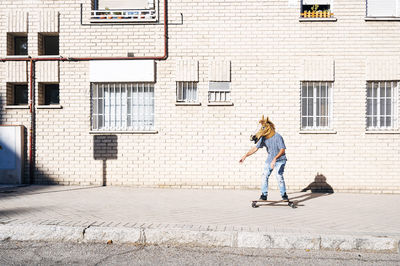 Man wearing horse mask while skateboarding on footpath against building in city during sunny day