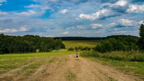 Rear view of teenage girl walking on field against sky