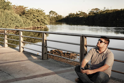 Man sitting on railing by lake against trees