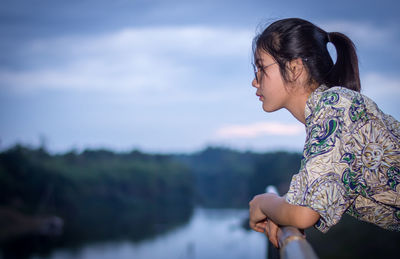 Side view of woman standing by lake against sky during sunset