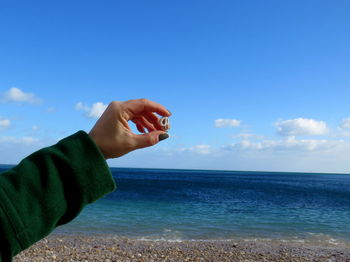 Cropped image of woman holding shell at beach against sky