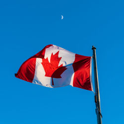 Low angle view of canadian flag against blue sky and moon