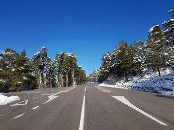 Road amidst trees against clear blue sky