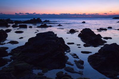 Rocks on beach against sky during sunset