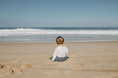 Rear view of boy sitting on beach against sky