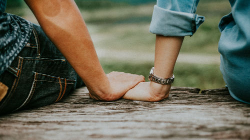 Cropped image of couple holding hands while sitting on bench