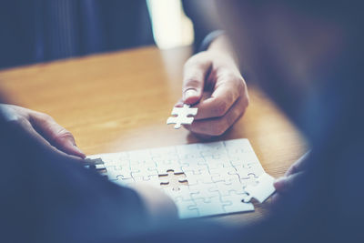 Cropped image of people playing jigsaw puzzle at home