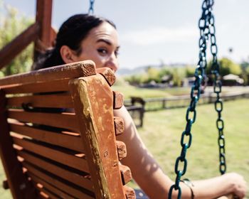 Portrait of young woman sitting on bench swing at public park