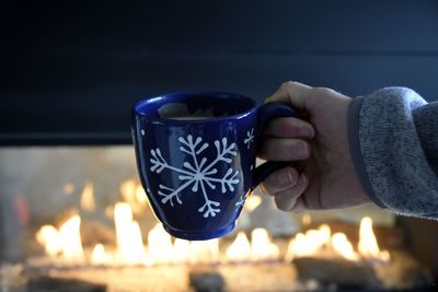 Cropped image of woman holding coffee cup against fireplace