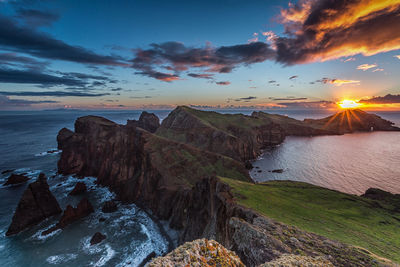 Scenic view of sea by rock formation against sky during sunset