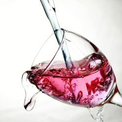 Close-up of red wine pouring over white background