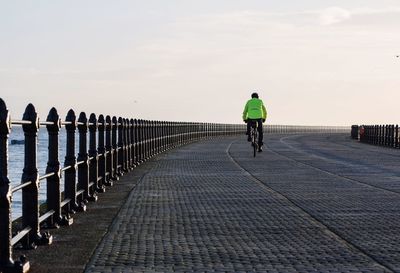 Rear view of man riding bicycle on bridge by sea against sky