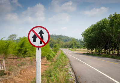 Road sign by trees against sky