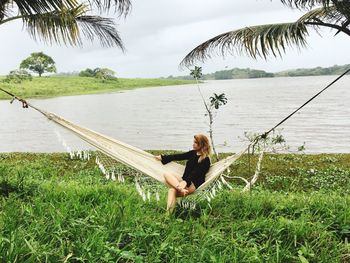 Thoughtful woman sitting on hammock by lake