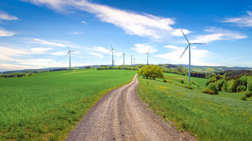 Road amidst field with wind turbines against sky