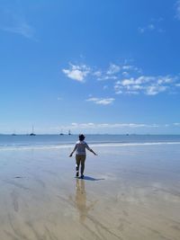 Rear view of man standing on beach against sky