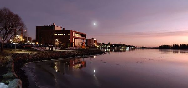 Illuminated buildings by lake against sky at night