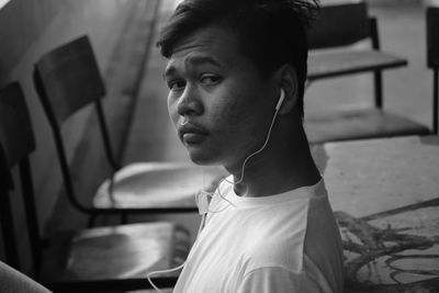 Portrait of young man listening to music through in-ear headphones on chair