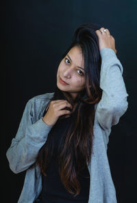 Portrait of beautiful young woman standing against black background