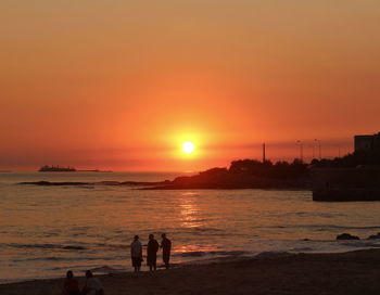 People standing at beach against sky during sunset