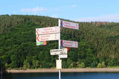 Information sign by trees against sky