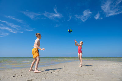 Boy playing on beach against blue sky