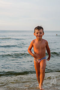 Portrait of shirtless boy standing in sea against sky