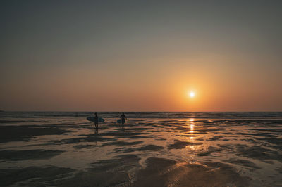 Silhouette people on beach against sky during sunset