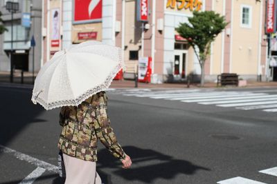 Midsection of woman with umbrella walking on road in city