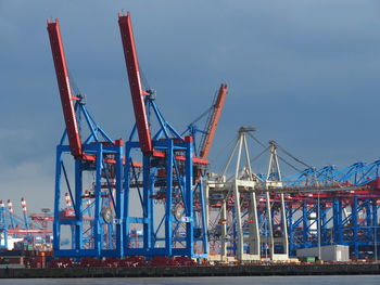Cranes at harbor against sky
