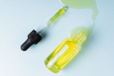 Face beauty oil spilled out of the dropper bottle on blue background. concept of skin care serum. 