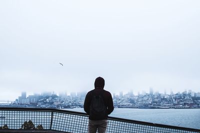 Rear view of man looking at buildings in city against clear sky