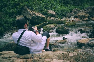 Rear view of man photographing stream in forest