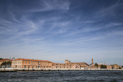 Buildings by river against blue sky