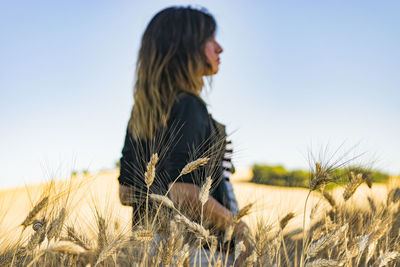 Side view of young woman in field against clear sky