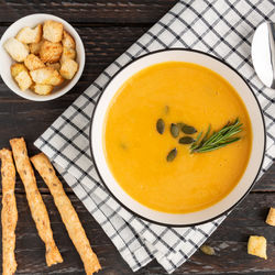 A bowl with pumpkin cream soup with grossini bread sticks and resemary on dark wooden background.