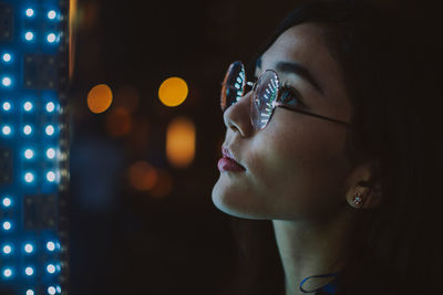 Close-up of young woman standing against illuminated city at night