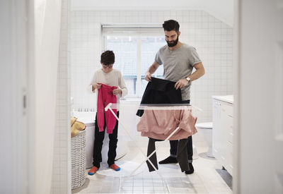 Son and father drying clothes on rack at home