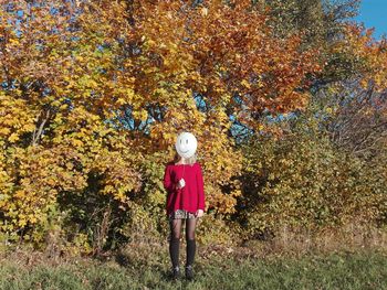 Full length of woman with face covered by balloon against trees on field during autumn