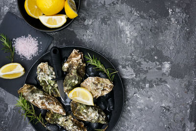 On the gray table there is a serving of black dishes with fresh oysters and lemon