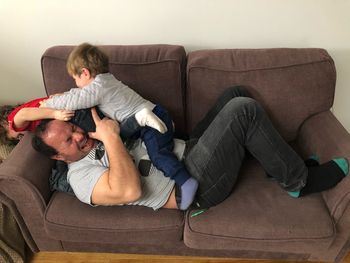 High angle view of father playing with sons while lying on sofa at home