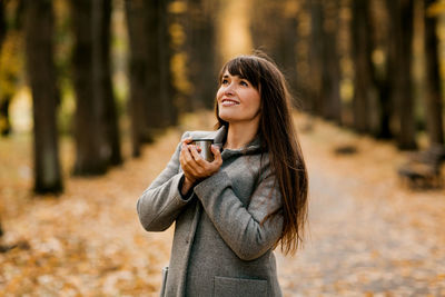 Portrait of a beautiful young woman drinking a hot drink while walking in an autumn park