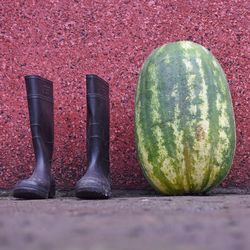 Rubber boots by watermelon against wall