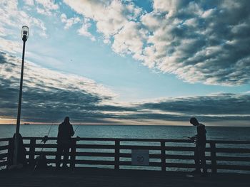 Silhouette people looking at sea against sky