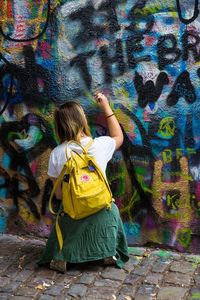 Rear view of woman standing against graffiti wall