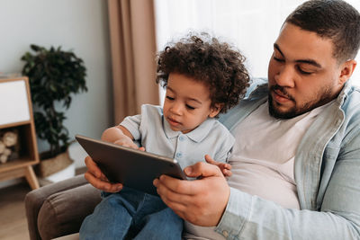 Father and son looking at digital tablet while sitting on sofa