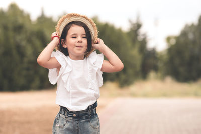 Funny cute child girl 3-4 year old holding straw hat wear white top and denim shorts over nature